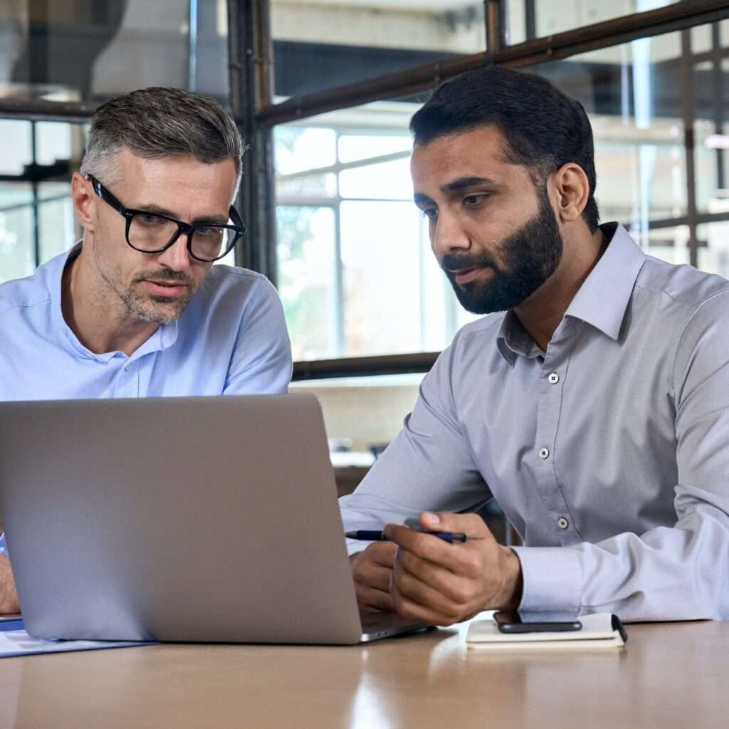 Two business men analysts discussing data management using laptop computer.