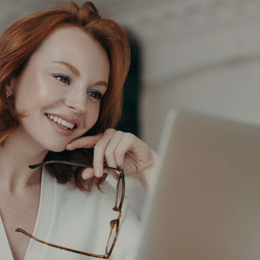 Female copywriter with red hair, concentrated on remote job, looks at laptop screen